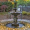 Square frame Beautiful tiered fountain on a garden with lush trees and plants in autumn