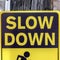 Square frame Black and yellow Slow Down Kids And Pets At Play sign against gray wooden pole