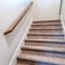 Square frame Carpeted indoor staircase of home with brown handrail against white side wall