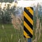 Square frame Close up of black and yellow diagonal stripes road sign beside barbed wire fence