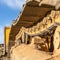 Square frame Close up of the dirty track pad and rollers of a yellow excavator on a sunny day