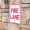 Square frame Fire Lane sign on stone retaining wall amid thick fresh snow on a hill in winter