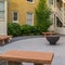 Square frame Fire pit on circular pavement with stone benches against building exterior