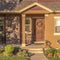 Square frame Home with pathway leading to gabled entrance of the front porch with brown door