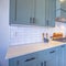 Square frame Kitchen with white counter top and bluish gray cabinets against tile backsplash