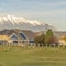 Square frame Narrow road and grassy terrain against homes and snowy mountain on a sunny day