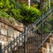 Square frame Outdoor staircase with stone steps and black metal railing against a fence