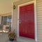 Square frame Shiny red wooden front door of a home with wicker chairs on the sunlit porch