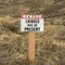 Square frame Sign that reads Beware Snakes May Be Present on a grassy mountain