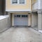 Square frame Snowy home with gray glass panelled garage door and stairs going to porch