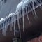 Square frame Spiked icicles at the edge of pitched gray roof with clumps of snow in winter