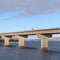 Square frame Truck travelling on a beam bridge over lake against rugged land and cloudy sky