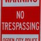 Square frame Warning No Trespassing sign against a metal pole and rough brick wall