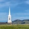 Square frame White steeple and rooftop of a church viewed from a grassy hill on a sunny day