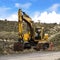 Square frame Yellow excavator and orange traffic delineator post beside a mountain road