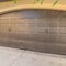 Square Garage door with an arched design against the concrete and brick wall of a home