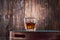 A square glass of whiskey on the rocks sits on a tray against an old wooden wall