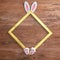 Square gold frame, bunny ears and paws, on a wooden background. Text space. Top view. Minimal style. Easter