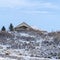 Square Hill top blanketed with white snow with view of gabled homes against blue sky