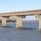 Square Huge truck travelling on a bridge that crosses a blue lake under cloudy sky