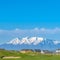 Square Lush grassy terrain with a view of lake and snow capped mountain under blue sky