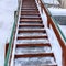 Square Outdoor stairs with grate metal treads and green handrail on snowy winter hill