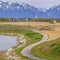 Square Paved pathway curving along the rocky and grassy lake shore under cloudy sky