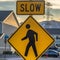 Square Pedestrian crossing road sign against houses vehicles mountain and cloudy sky