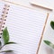 A square photo of an empty open lined notebook with green leaves