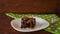 A square piece of chocolate brownie on a plate, poured stringy salted caramel. A green napkin in a white dot and a