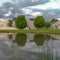Square Pond with reflection of multi storey homes lush trees and cloud filled sky