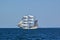 Square-rigged white sailing ship at sea with a distant shore in the background