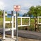 Square Road with white gate and sign post against trees and grassy field on a sunny day