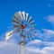 Square Shiny steel windpump against a vibrant blue sky with cottony clouds