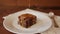 Square slice of chocolate brownie on a plate, on a wooden background with a napkin and spoon - poured viscous salted