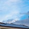 Square Solar panels installed on the roof of a home with white horizontal wall siding