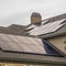 Square Solar panels mounted on the dark pitched roof of a home under cloudy gray sky