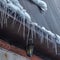 Square Spiked icicles at the edge of pitched gray roof with clumps of snow in winter