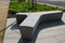 In the square stands a gray, white bench made of artificial stone. Pouring concrete in the shape of T or Y. Perennial beds bloomin