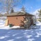 Square Storage shed with hip roof and brown wooden wall against snow and cloudy sky