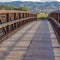 Square Sunlit wooden deck and metail railing of bridge over lake with mountain view