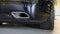 Square tailpipe at the rear right side of a black sports car. Very low plan. The rear bumper, wheel and tailpipe of the packed