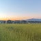 Square Vast terrain with green grasses against houses mountain and blue sky at sunset