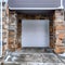 Square White panelled garage door of home with gray siding and stone exterior wall