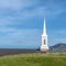 Square White steeple and rooftop of a church viewed from a grassy hill on a sunny day