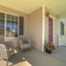 Square Wicker armchairs on the sunlit front porch of home with brown front door