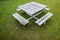 Square wooden picnic table with four benches, on a rain-soaked lawn