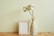 Square wooden picture frame and vase of soft cotton branch on wooden table. ivory wall background. blank message card, memo space