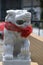 A squatting chinese guardian lion made of white stone wearing a red ribbon around its neck