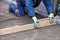 A squatting worker manually cleans and levels the sand base with a wooden plank for even tiling on the sidewalk